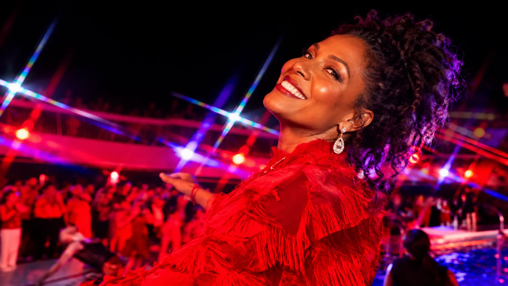 A Black woman celebrating in a red fringed outfit under vivid red and violet party lights